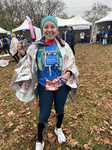 A woman in a National Brain Tumor Society running bib holds up a half-marathon medal after completing her race.