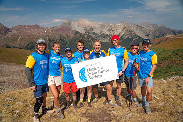 How to fundraise for brain tumor research can look like a group of adults in Gray Nation Endurance jerseys posing for a photo on a mountainside with a banner that reads "In Support of National Brain Tumor Society."