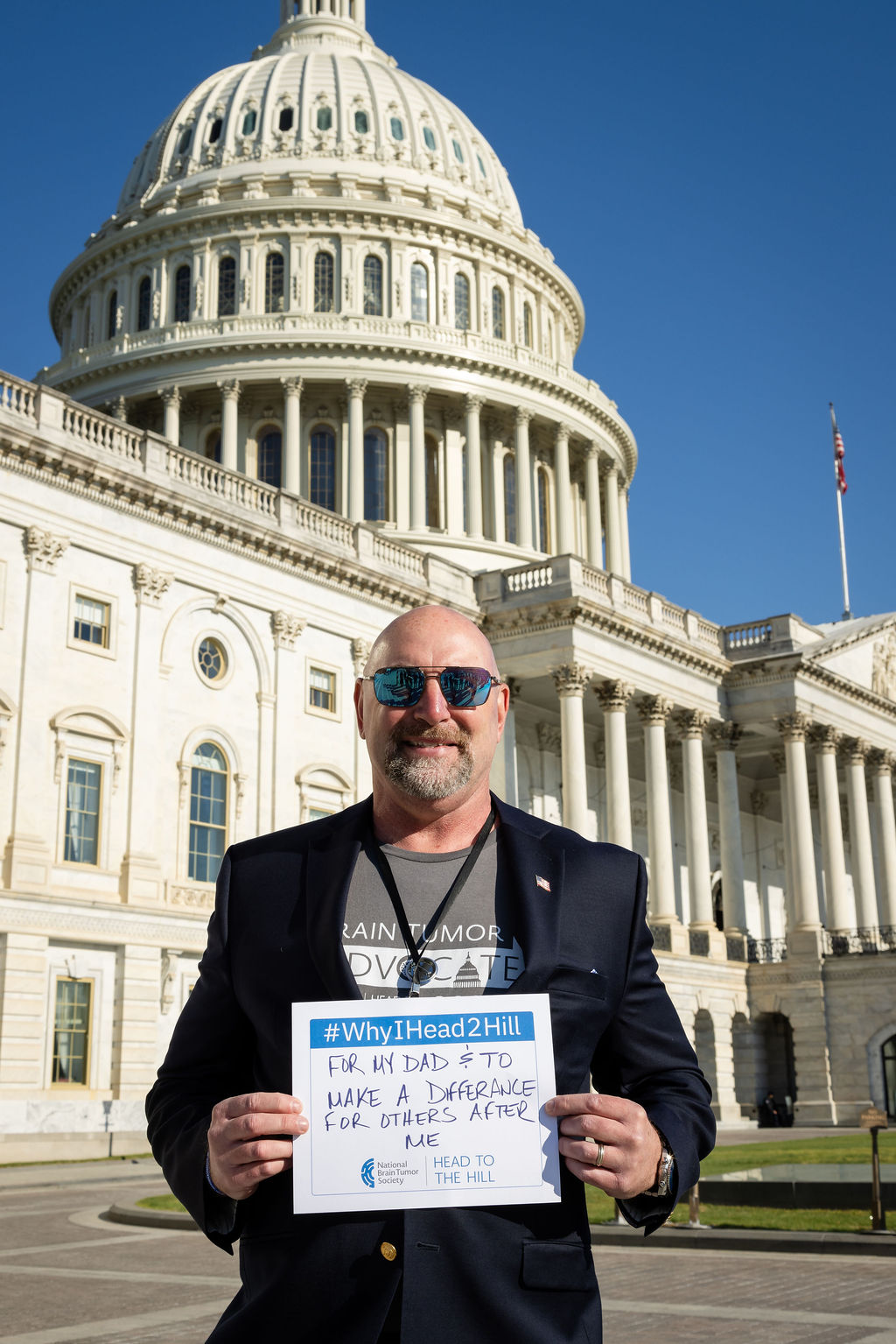 A man stands in front of the Capitol holding a sign about why he Heads to the Hill for the brain tumor community.