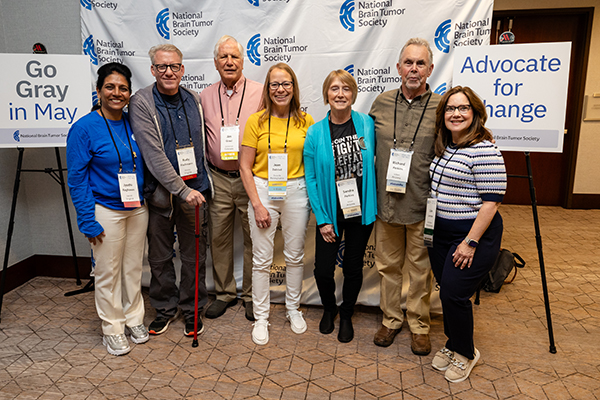 Seven people stand for a group photo in front of an NBTS backdrop at an event. Thanks to brain tumor research advocacy, they help shape research.