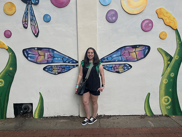 A woman, who is a spinal ependymoma survivor, stands in front of a butterfly mural.