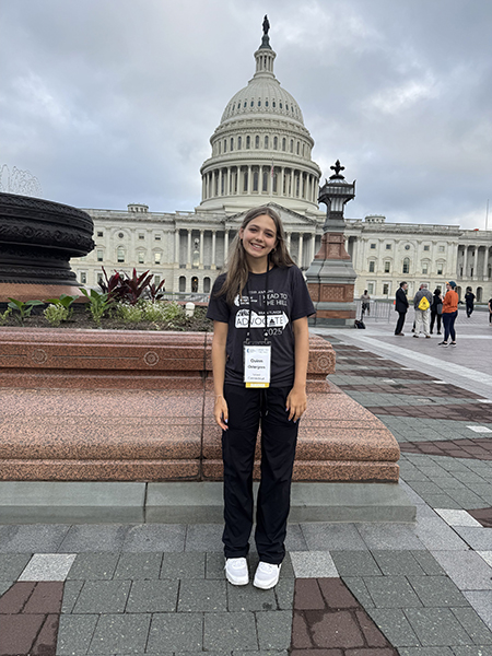 A teenage girl, who is a JPA survivor and pediatric brain tumor advocate, stands in front of the Capitol wearing her Head to the Hill t-shirt.