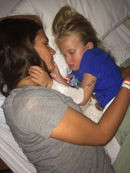 A mom rests in a hospital bed alongside her young daughter. Biomarker testing unlocked answers for this family.