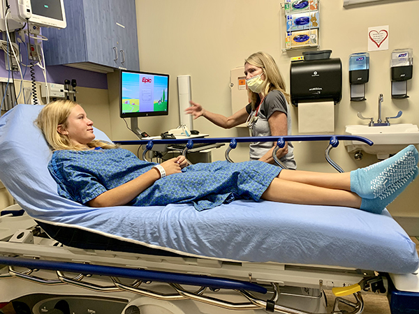 A teenage girl with blonde hair lays in a hospital bed, prepped for brain surgery. Biomarker testing unlocked answers for her and her family.