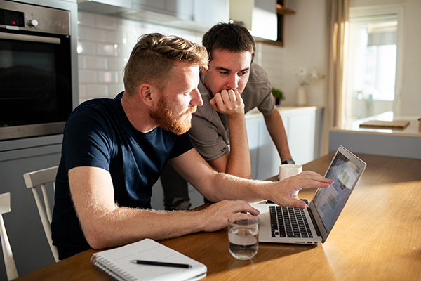 Close up of two adult men looking at a laptop on a kitchen counter.