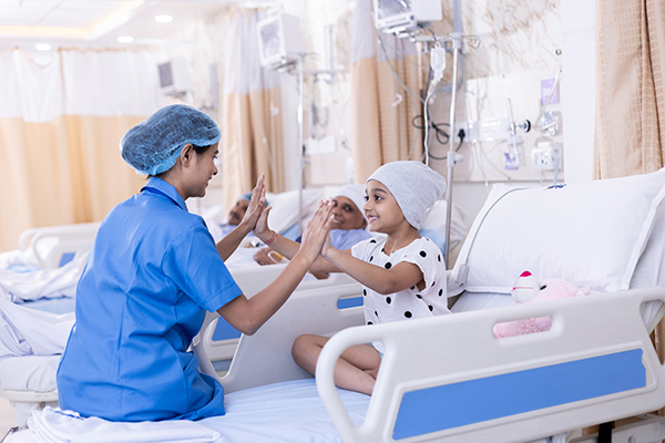 Little girl patient with medulloblastoma playing with nurse sitting on bed at hospital