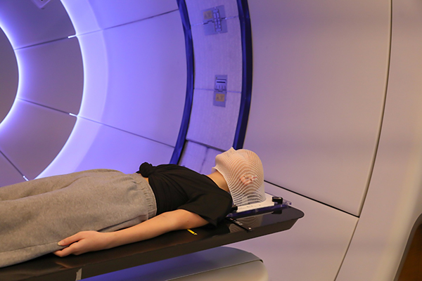 Medulloblastoma child patient lying on positioning bed with fixing mask on her head in proton radiation treatment room
