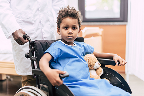 Portrait of pensive Black boy with medulloblastoma in wheelchair looking away in hospital