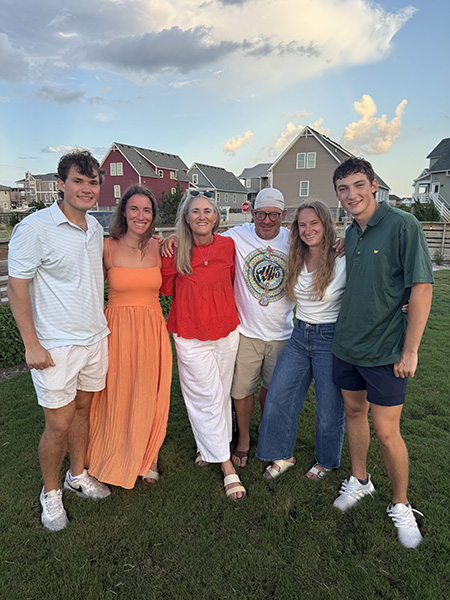 A family of 6 with four young adult children and their two parents pose for a photo in front of beach houses at the Outer Banks.